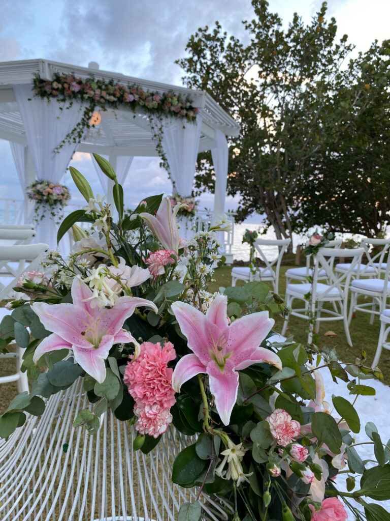 Romantic outdoor wedding ceremony setup with pink florals and ocean views at sunset.