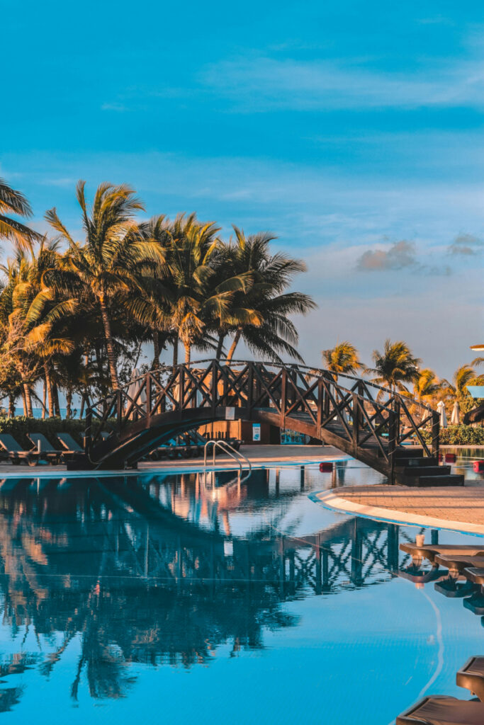 Tropical resort pool with wooden bridge and palm trees, calm and relaxing vacation setting