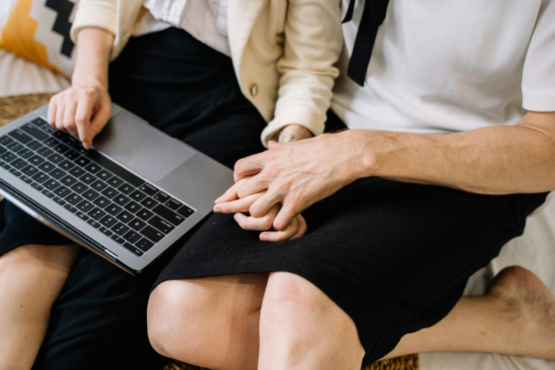 Couple holding hands while planning a romantic honeymoon together on a laptop at home.