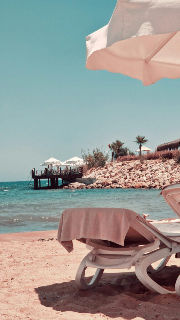 Relaxing beach lounge chairs beside clear ocean water at a peaceful tropical honeymoon resort destination.