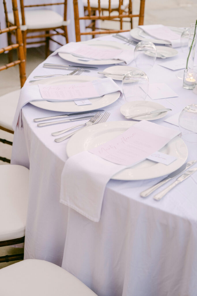 Elegant wedding reception table setup with white linens, silver flatware, and soft blush menus.