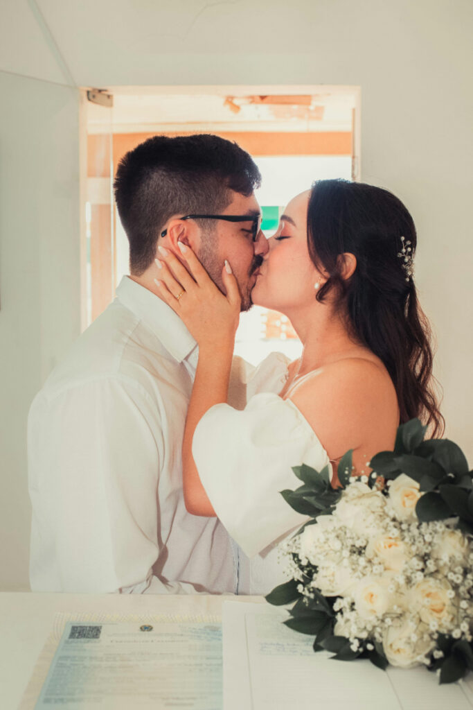 Bride and groom sharing a kiss before their weddings in Mexico celebration while holding a white floral bouquet.