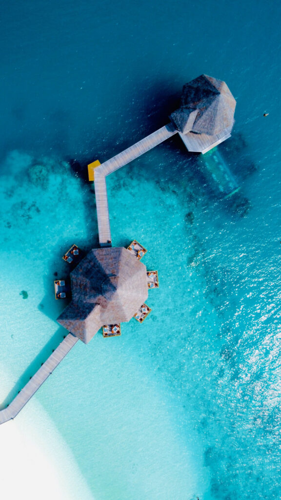 Aerial view of an overwater pavilion surrounded by crystal-clear turquoise water and wooden walkways.
